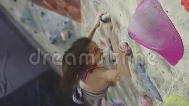 年轻女子攀岩者正在攀岩健身房里攀岩。 苗条美丽的女人在室内攀岩墙上锻炼